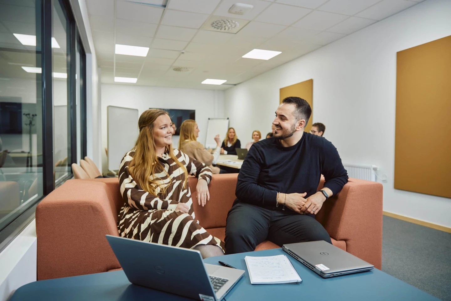 Två kollegor samtalar i en soffa i mötesrum.