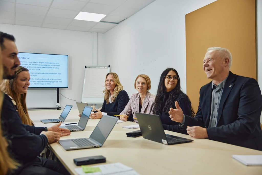 Kollegor i möte runt ett konferensbord med datorer.