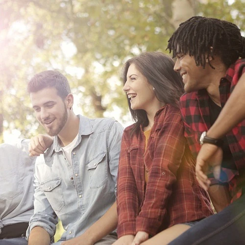 Grupp unga människor som skrattar tillsammans utomhus.