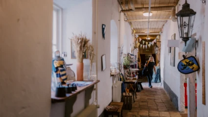 En ljus korridor i Tomarps Kungsgård fylld med hantverk och utställningsföremål, där en besökare rör sig genom miljön.