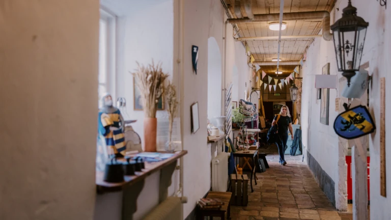 En ljus korridor i Tomarps Kungsgård fylld med hantverk och utställningsföremål, där en besökare rör sig genom miljön.