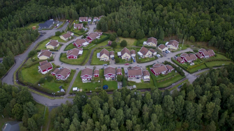 Ett lugnt bostadsområde omgivet av skog, med röda och gula villor längs slingrande gator i grön miljö.