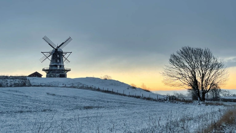 Bräcke mölla i vinterskrud, där den gamla kvarnen står på en höjd mot en färgsprakande solnedgång.