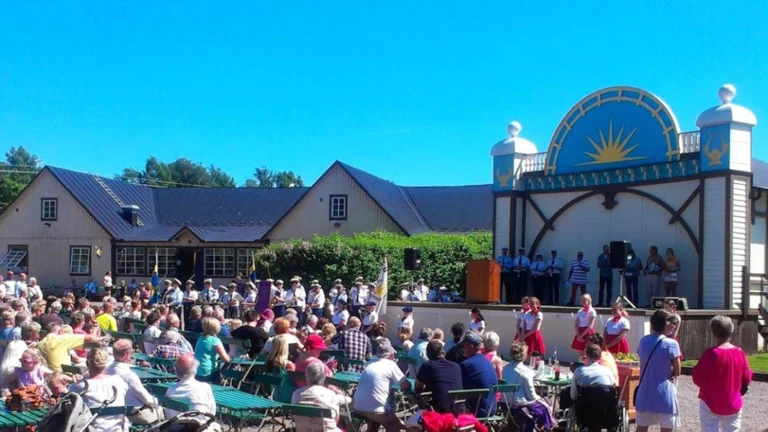 En livlig sommardag i folkparken med publik, scenframträdanden och gemenskap i klassisk folkparksmiljö.