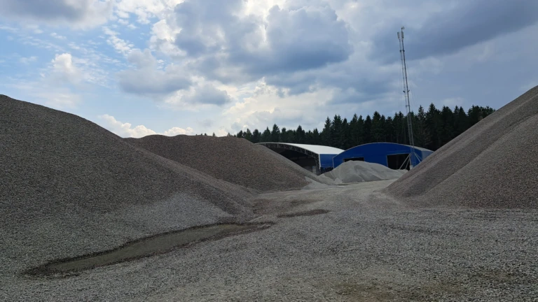 Ett grustag vid Bjärrsgård med stora högar av stenmaterial och maskiner i bakgrunden, omgivet av natur och skog.