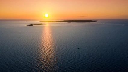 Solen speglar sig i det stilla vattnet när den går ner bakom Hallands Väderö, en vy i mjuka orange toner.