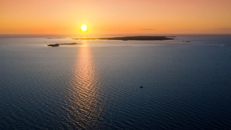 Solen speglar sig i det stilla vattnet när den går ner bakom Hallands Väderö, en vy i mjuka orange toner.