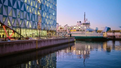 En ForSea-färja ligger förtöjd intill ett glasbeklätt kontorshus i Helsingborg medan ljusen speglar sig i vattnet.