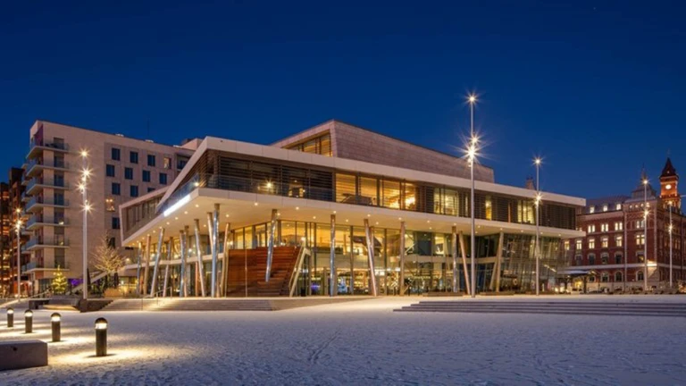 Det moderna konferenshotellet i Helsingborg lyser upp mot den blå kvällshimlen, omgivet av stadens historiska byggnader.