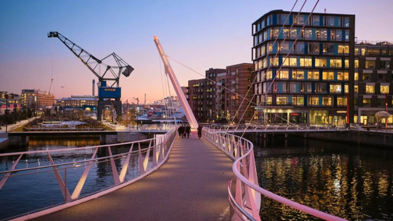 Den moderna hamnmiljön i Helsingborg med gångbro, vatten, kontorshus och kran i kvällsljus – en mötesplats vid havet.