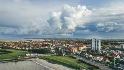 Utsikt över kuststaden Höganäs med strand, bostäder och hamn, inramad av dramatisk himmel och vida vyer.