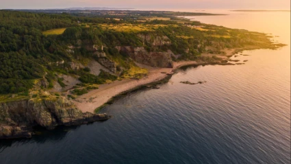 En dramatisk kuststräcka med klippor och strand som badar i gyllene kvällsljus vid Hovs Hallar.