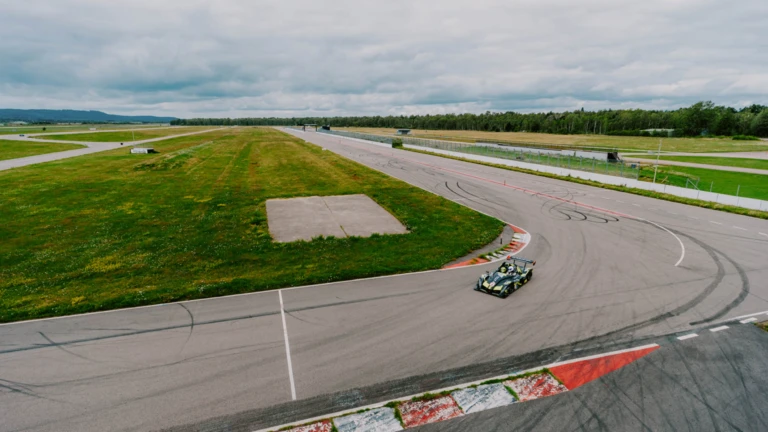 En sportbil tar kurvan på Ljungbyheds motorbana, omgiven av gröna fält och öppet landskap