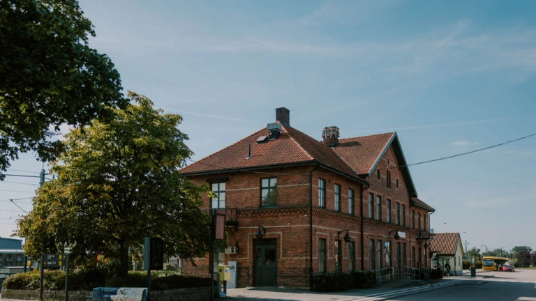 Klippans station med sin karaktäristiska tegelbyggnad och röda tak ligger vackert inbäddad i grönska.