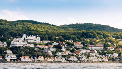 En pittoresk kustvy över Mölle där vita hus och röda tak klättrar upp längs Kullabergens sluttning mot grönskande skog.