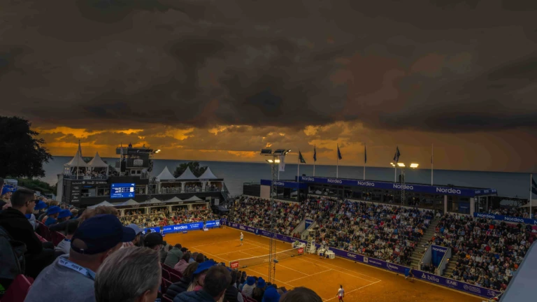 Publikfylld tennisarena under Nordea Open i Båstad, med intensiva matcher och spektakulär himmel över havet.