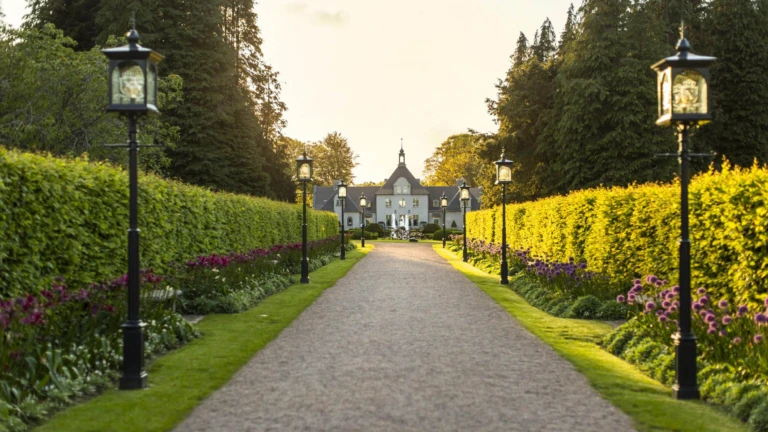 Den symmetriska entrén till Norrvikens Trädgårdar omgiven av prydliga rabatter och välklippta häckar i kvällssol.