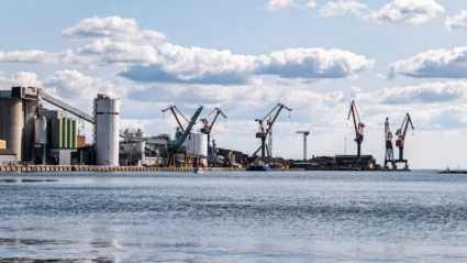 Industrihamn med flera lastkranar och lagringstankar längs kajen, där fartyg lastar och lossar gods.