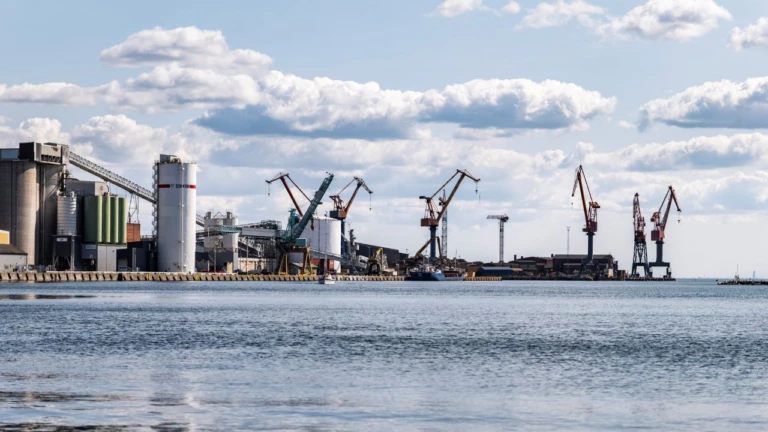 Industrihamn med flera lastkranar och lagringstankar längs kajen, där fartyg lastar och lossar gods.