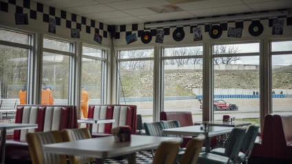 50-talsinspirerad servering vid Ring Knutstorp, med utsikt mot banan där tävlingar pågår utanför fönstret.