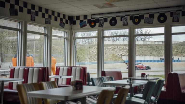50-talsinspirerad servering vid Ring Knutstorp, med utsikt mot banan där tävlingar pågår utanför fönstret.