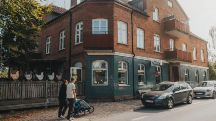 En solig dag i Röstånga där besökare strosar förbi ett kafé i ett charmigt tegelhus med hantverksbutik.