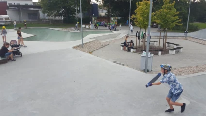 En livlig skatepark där barn och ungdomar åker skateboard och sparkcykel i betongrampens öppna ytor.