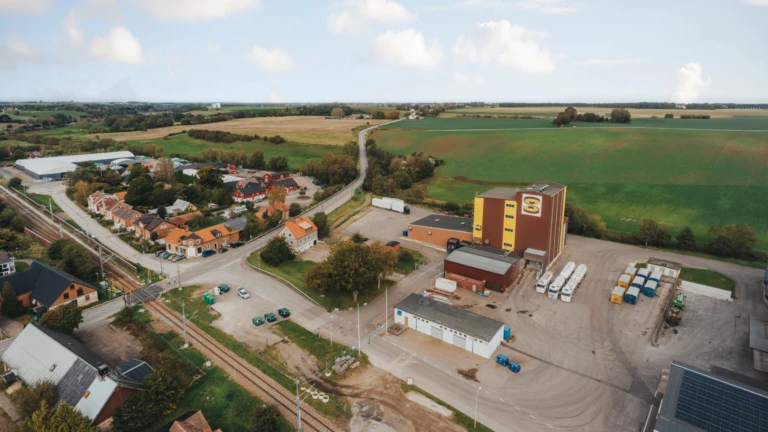 En lantlig vy över Tågarp i Svalövs kommun med fält, bostäder och en större industri- och logistikbyggnad.