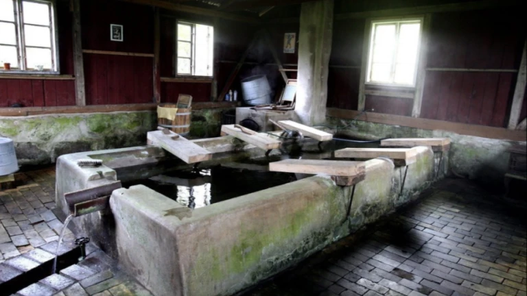 En historisk tvättstuga i Norra Vram med ångande vattenkar, stenväggar och tidstypiska redskap som visar äldre tvätttraditioner.