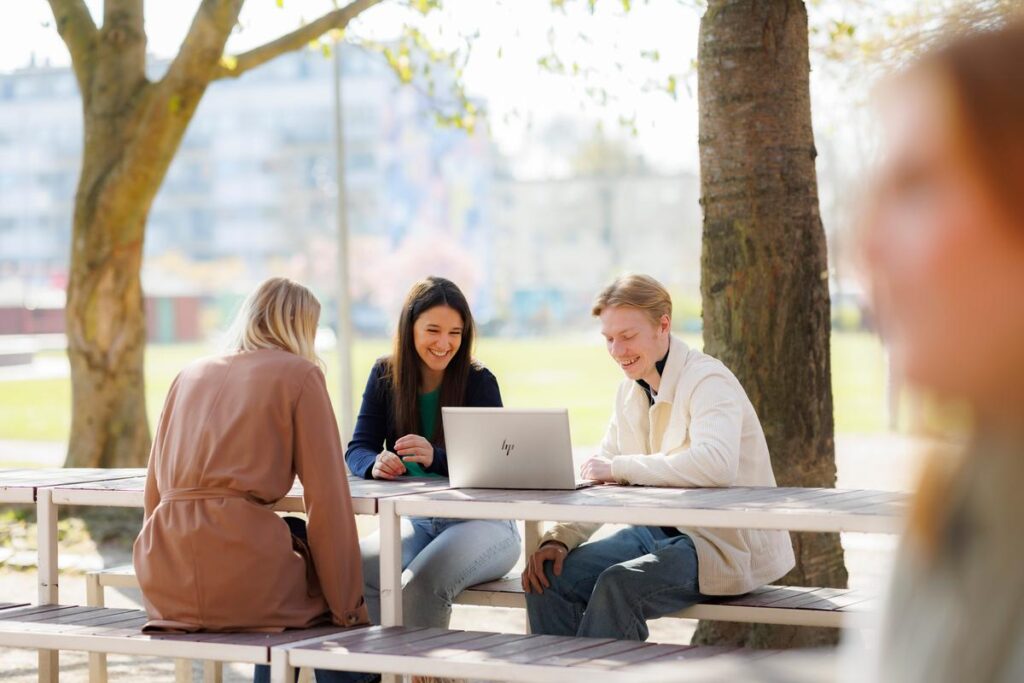 två kvinnor och en man som sitter vid ett bord utomhus. 