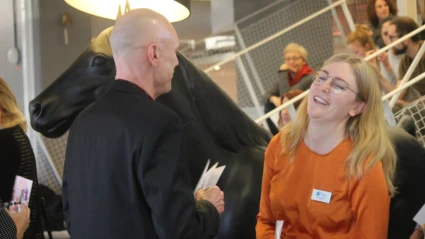 Avslappnat samtal under mingel där två deltagare skrattar tillsammans, med andra i bakgrunden.