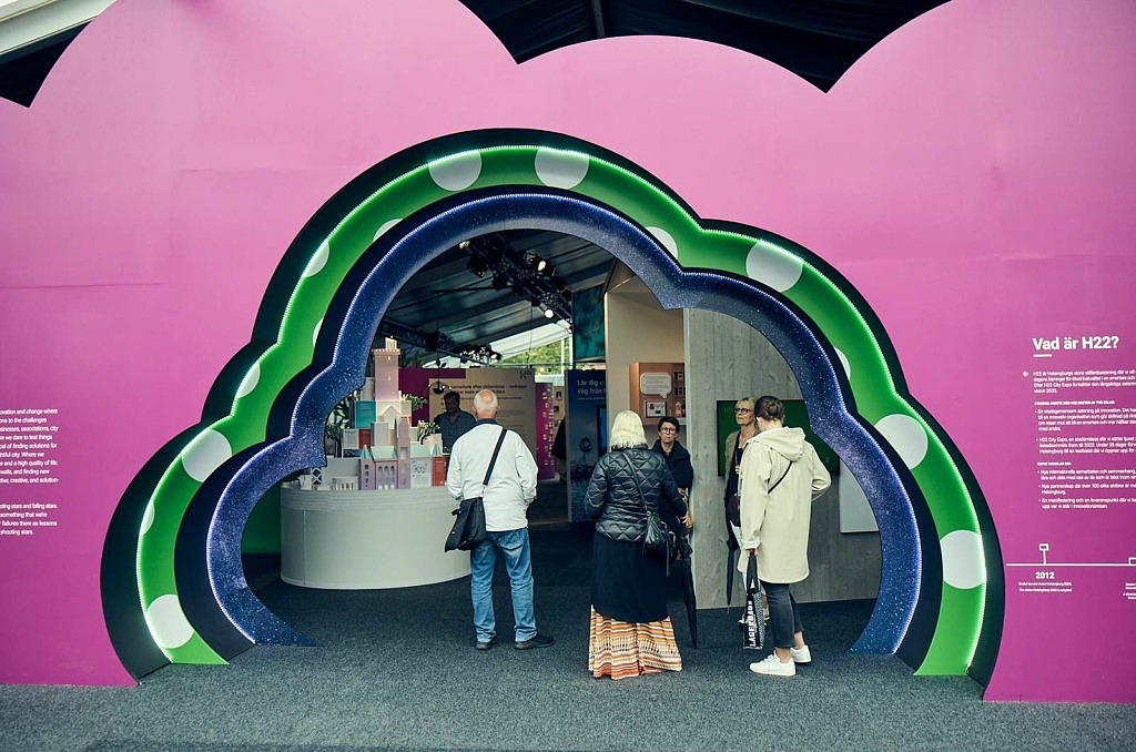 En molnformad vägg med en öppning i olika färger, där människor är på väg in i innovationsutställningen under H22
