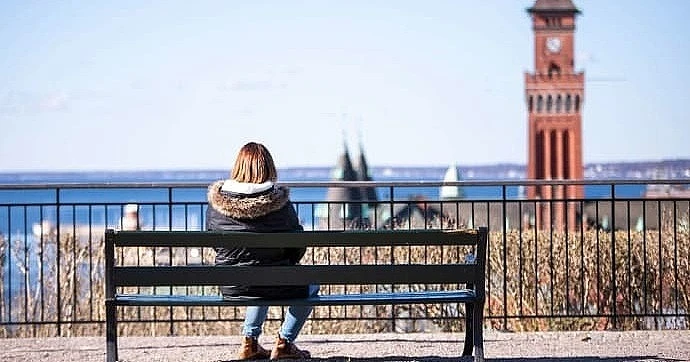 Flicka sitter ensam på bänk och blickar ut över Helsingborg och sundet.