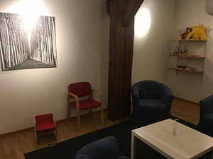Rummet innan renoveringen. Slitna blå fåtöljer, vita väggar och en liten barnstol.