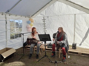 Två kvinnor sitter och spelar gitarr och sjunger i ett tält.