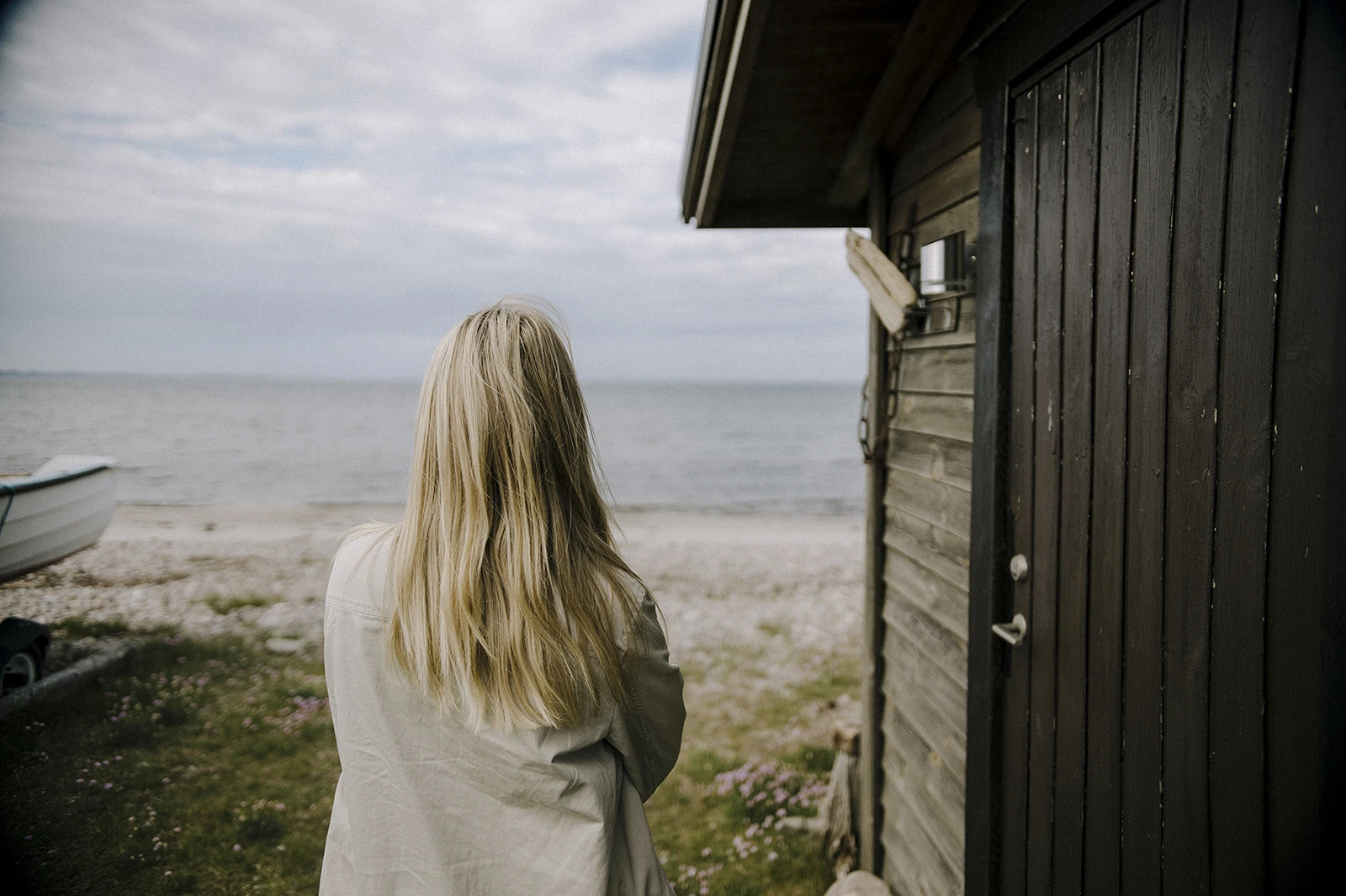 Kvinna står vid ett båthus och tittar ut över havet.