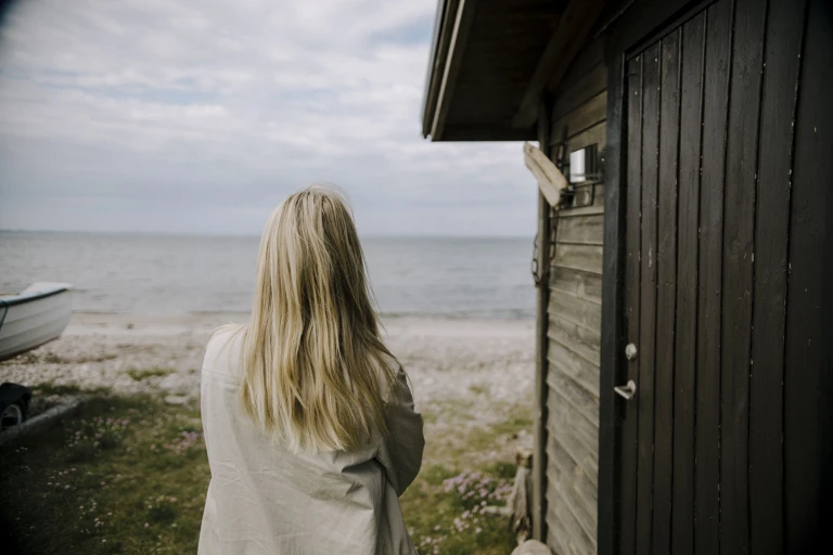 Kvinna står vid ett båthus och tittar ut över havet.