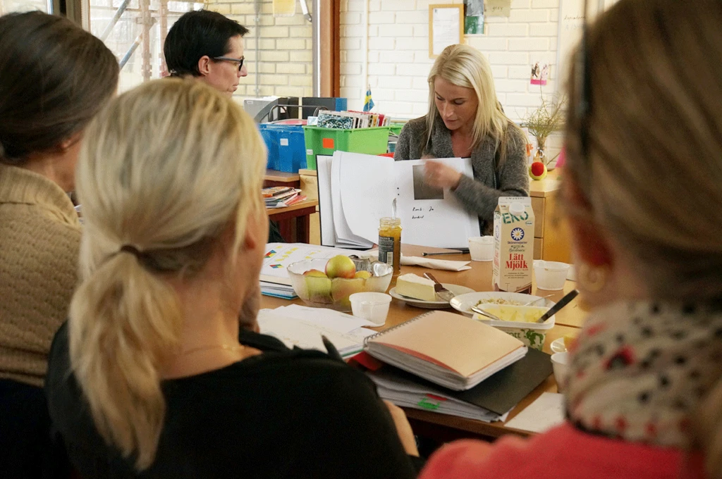 Pedagoger sitter runt ett bord och ev visar papper i en pärm