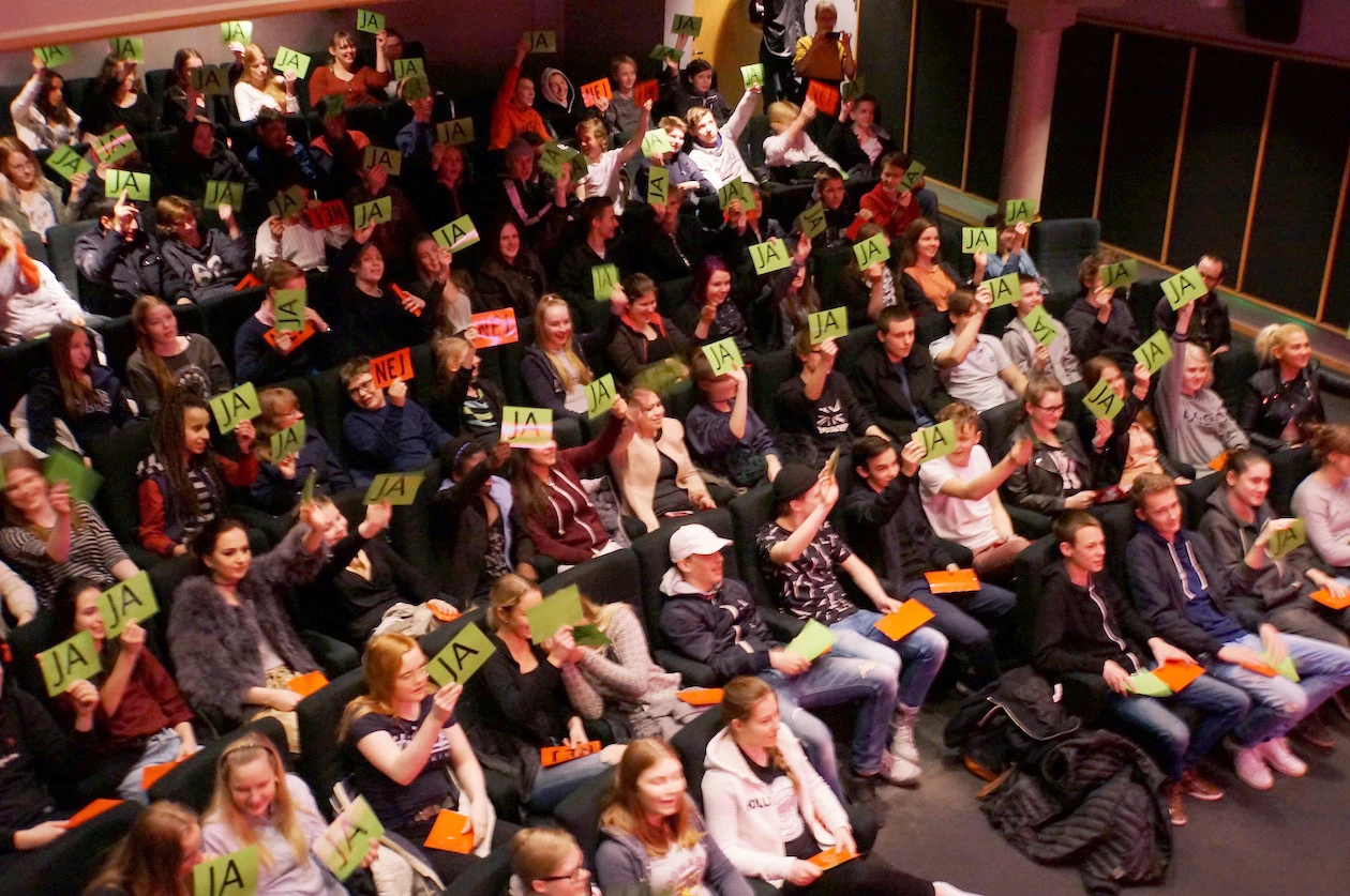 Fullsatt biosalong med elever som räcker upp röstkort