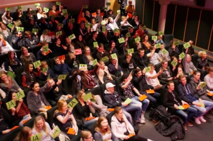 Fullsatt biosalong med elever som räcker upp röstkort