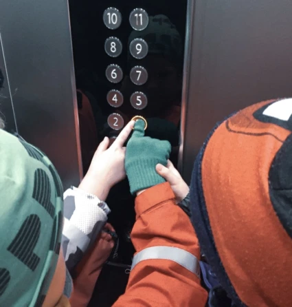 Panel med knappar i en hiss och två barnhänder som trycker på en knapp