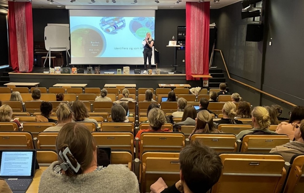 En person står på scen framför en sittande publik.
