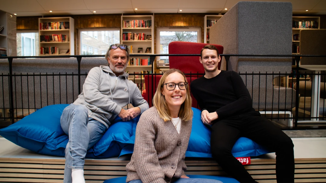 Tre personer sitter inne i ett bibliotek. Team värdegrund på Wieselgrensskolan.