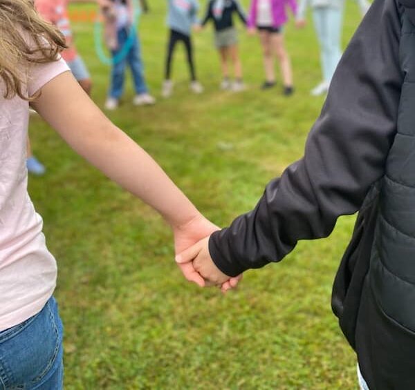 Elever håller varandra i handen och står i en stor ring tillsammans i parken