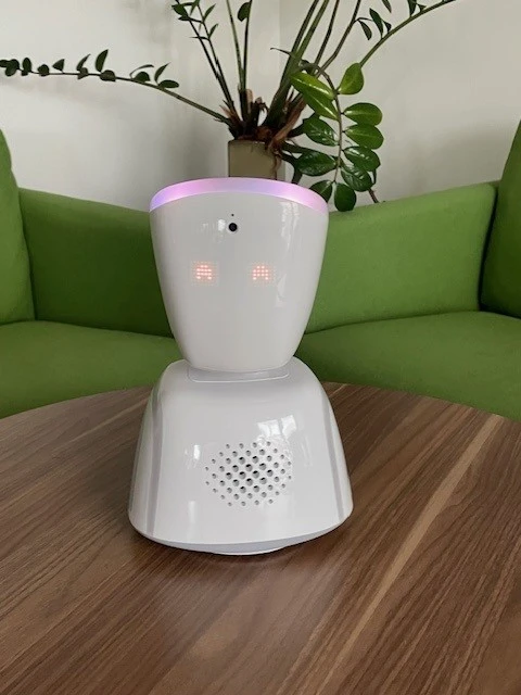 En vit robot med huvud och kropp. Den står på ett bord. ögonen lyser och ser glada ut. 