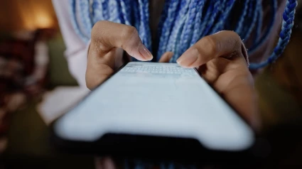 Närbild på händer som skriver på en smartphone, med skärmen upplyst och texten suddig i förgrunden.