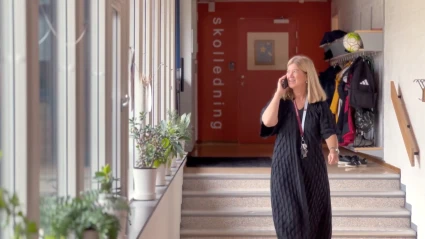 Rektor går i skolans korridor. Pratar i telefon.