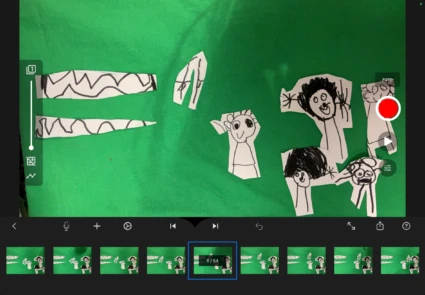 En skärmdump från ett filmredigeringsprogram på en iPad som visar utklippta pappersfigurer mot en grön bakgrund för stop-motion-animering.