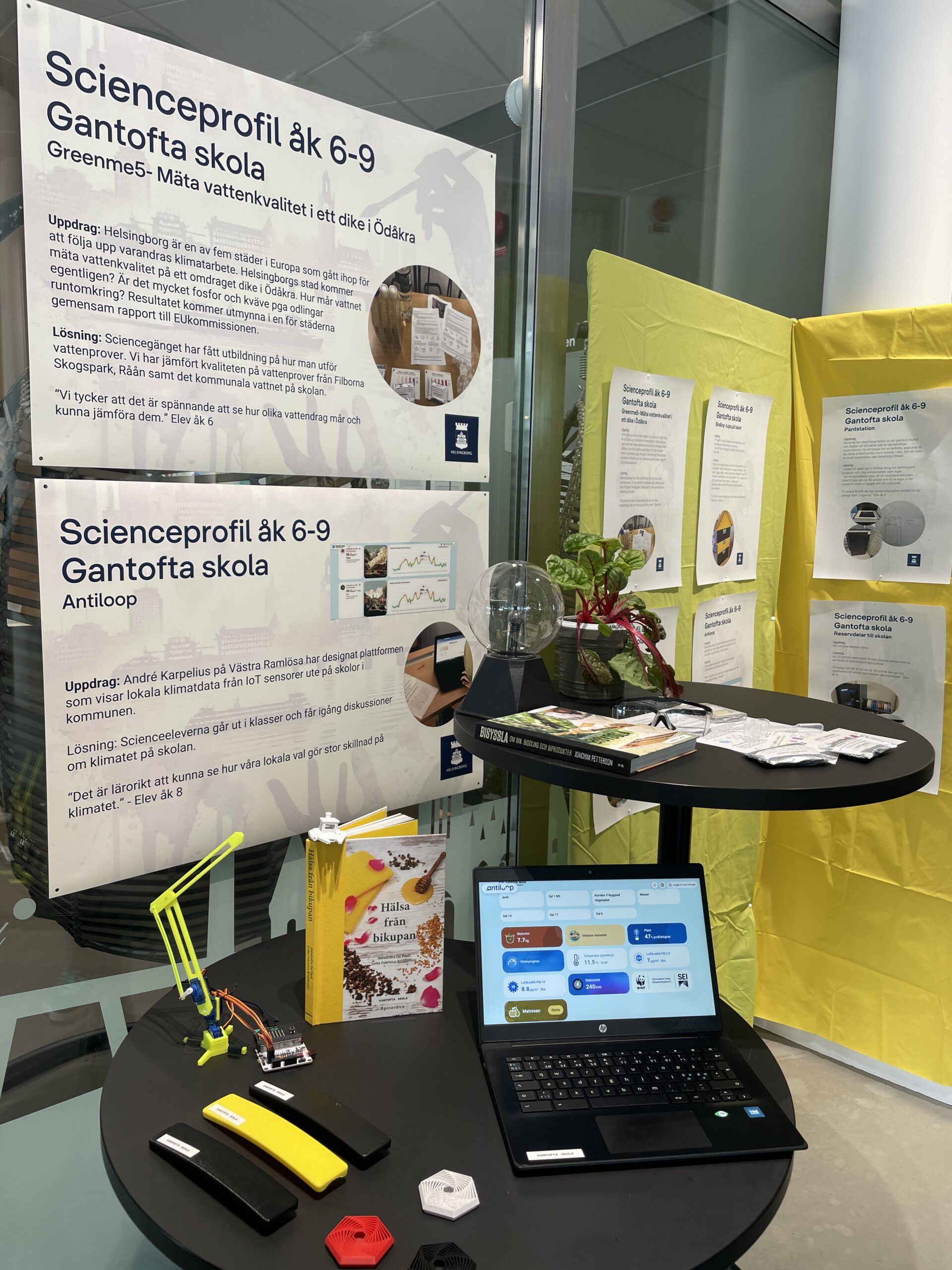 Ett bord med en bärbar dator som visar en datapanel, 3D-printade svarta och gula handtag till matsalsstolar och informationsskyltar från Gantofta skolas science-profil.