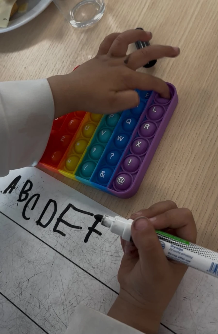 Ett barn deltar i en bokstavsaktivitet med en poppit-leksak och en whiteboard-penna, vilket uppmuntrar till lekfull inlärning av alfabetet.